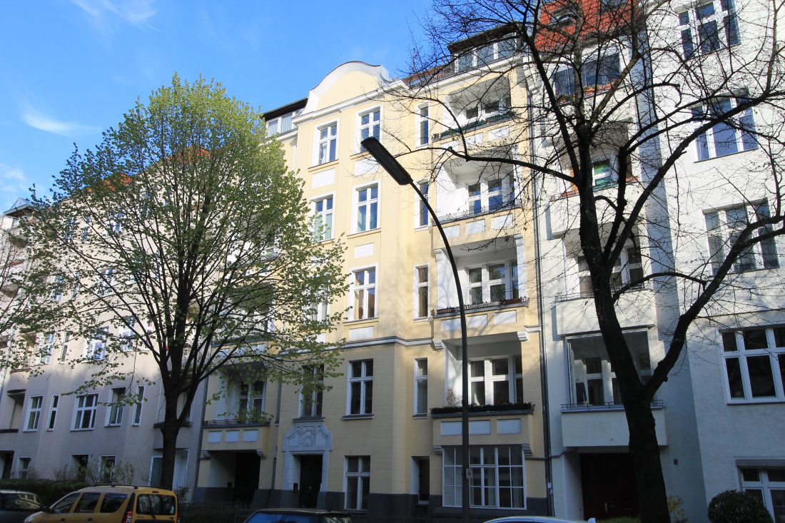 Hellgelbes Altbauhaus an einer Straße mit Bäumen und einer Laterne