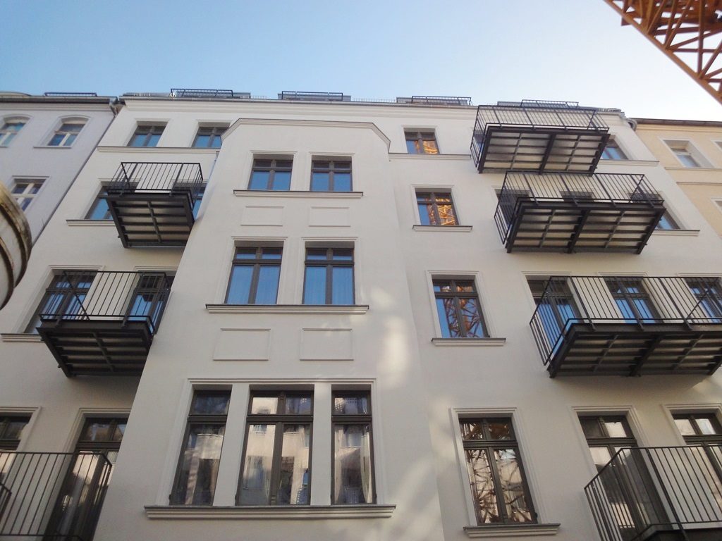 Weiß verputzte Altbaufassade mit dunklen Stahlbalkonen, von unten gesehen