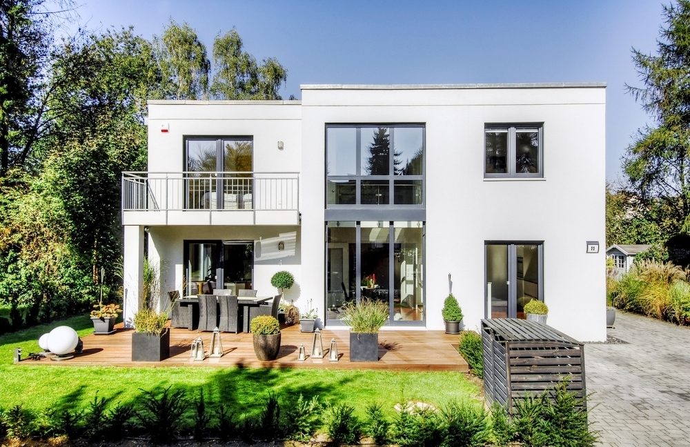 Weißes Einfamilienhaus mit Balkon und Holzterrasse, davor ein Rasen